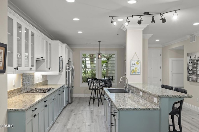 kitchen with light wood-type flooring, stainless steel appliances, sink, white cabinetry, and decorative light fixtures