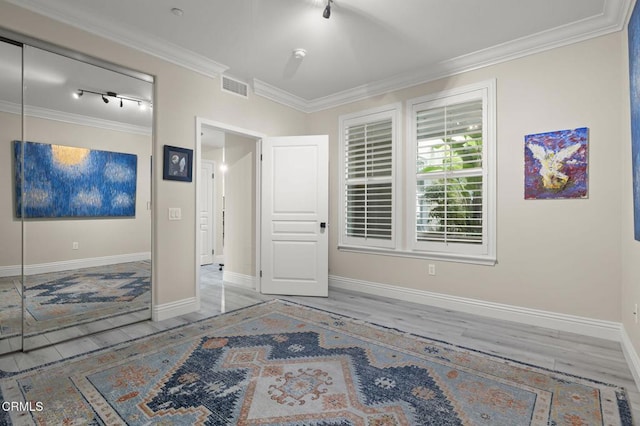 unfurnished bedroom with a closet, ornamental molding, light hardwood / wood-style flooring, and track lighting