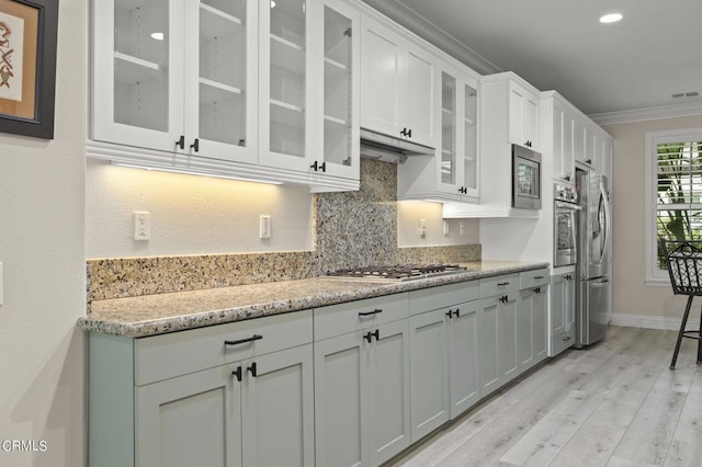 kitchen with light stone counters, white cabinets, ornamental molding, light hardwood / wood-style flooring, and stainless steel appliances