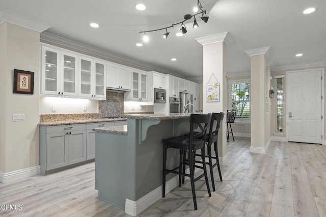 kitchen featuring an island with sink, light stone counters, a breakfast bar area, appliances with stainless steel finishes, and decorative columns