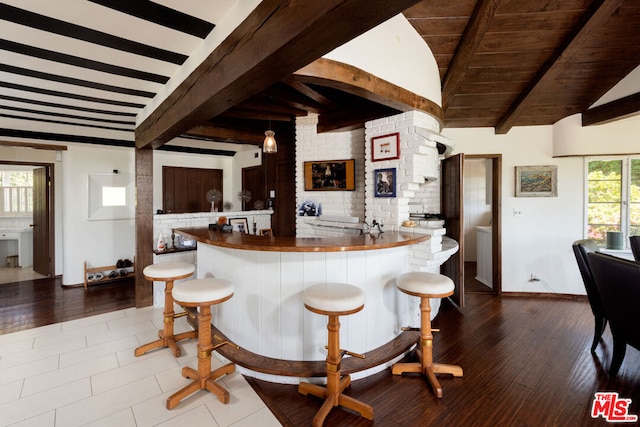 kitchen with a kitchen bar, kitchen peninsula, hardwood / wood-style floors, and lofted ceiling with beams