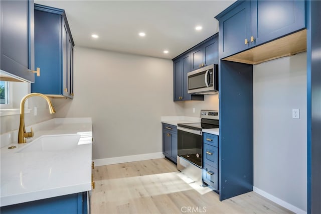 kitchen with appliances with stainless steel finishes, blue cabinets, and light hardwood / wood-style flooring