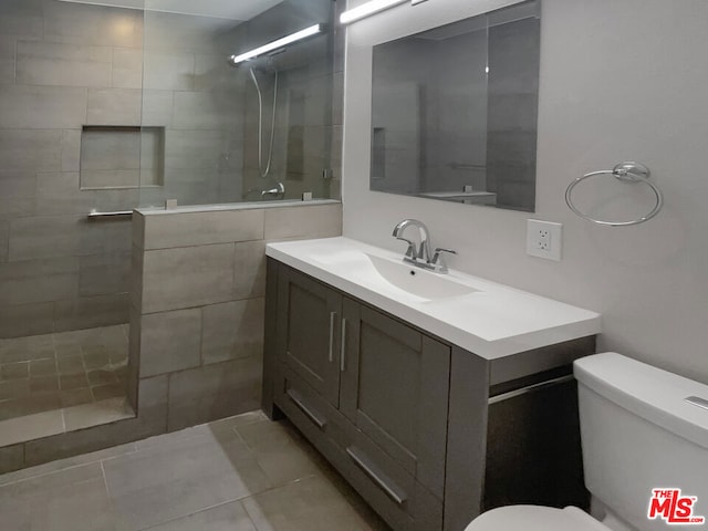 bathroom with toilet, a tile shower, vanity, and tile patterned floors