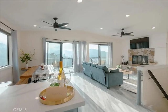 living room with ceiling fan, a healthy amount of sunlight, and a stone fireplace