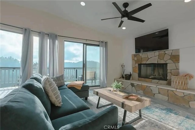 living room featuring a stone fireplace, ceiling fan, and a healthy amount of sunlight