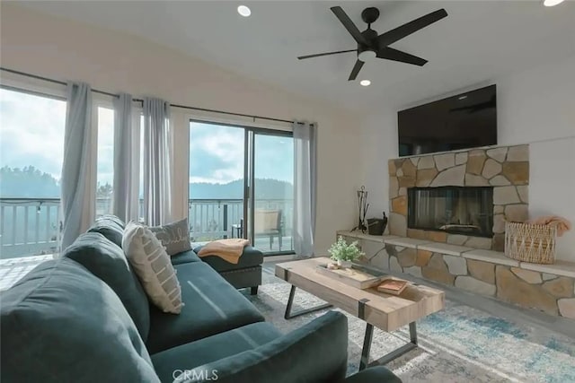 living room with a stone fireplace, a wealth of natural light, and ceiling fan