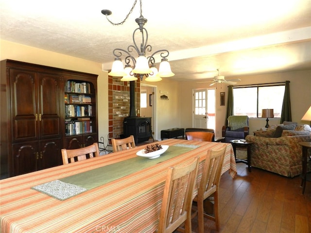 dining area with a wood stove, dark hardwood / wood-style flooring, and ceiling fan with notable chandelier