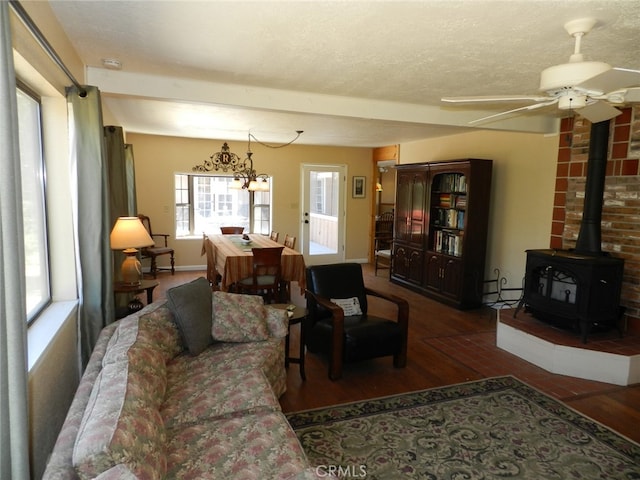 living room with beam ceiling, ceiling fan, a textured ceiling, wood-type flooring, and a wood stove