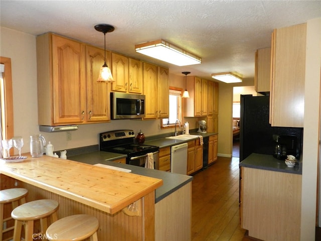 kitchen featuring kitchen peninsula, hanging light fixtures, dark hardwood / wood-style flooring, sink, and stainless steel appliances