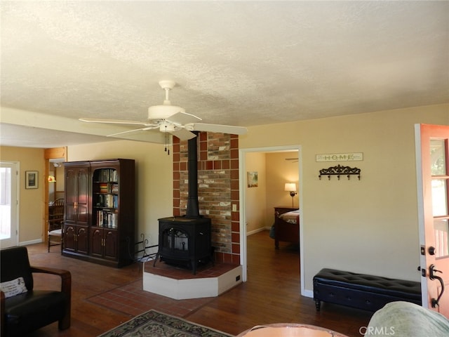 living room featuring a wood stove, dark hardwood / wood-style floors, a textured ceiling, and ceiling fan