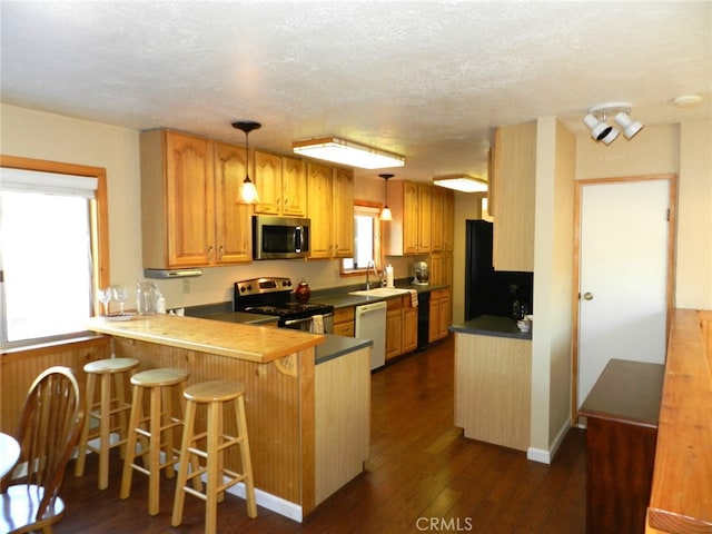 kitchen with kitchen peninsula, a breakfast bar area, appliances with stainless steel finishes, dark wood-type flooring, and pendant lighting