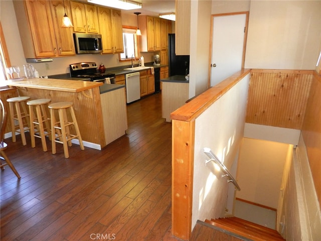 kitchen featuring kitchen peninsula, dark hardwood / wood-style flooring, a breakfast bar, sink, and stainless steel appliances