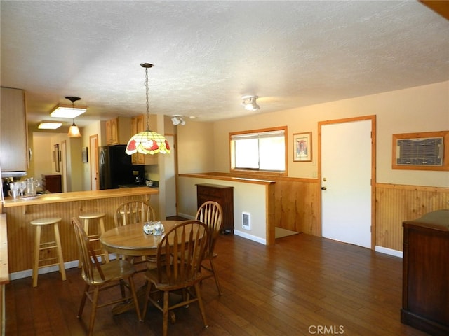 dining area with a textured ceiling, wooden walls, and dark wood-type flooring