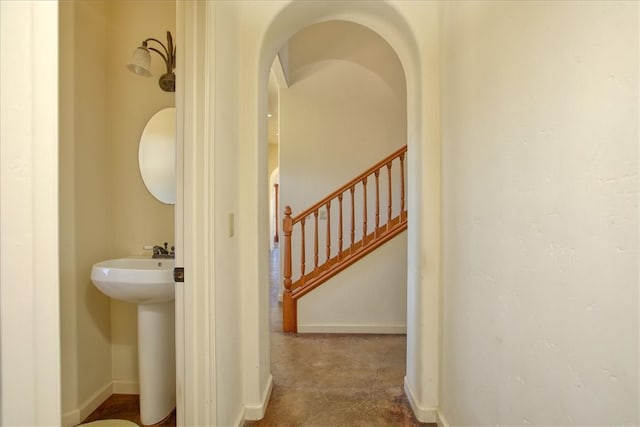 hall featuring baseboards, stairway, and arched walkways