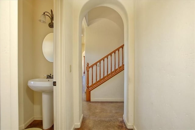 corridor with baseboards, arched walkways, stairs, and a sink