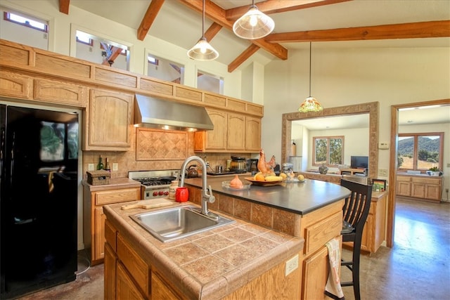 kitchen with pendant lighting, freestanding refrigerator, a sink, wall chimney range hood, and an island with sink