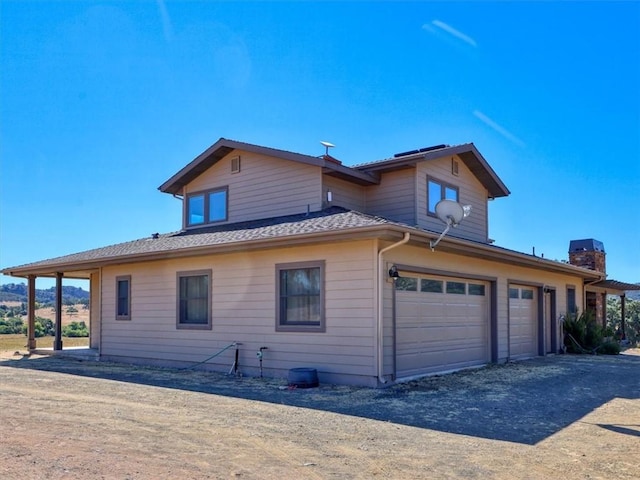view of side of property with a garage, a chimney, and dirt driveway