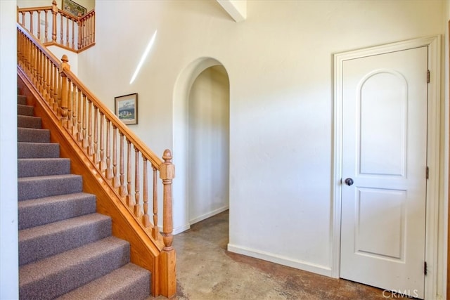 staircase with concrete flooring, arched walkways, and baseboards