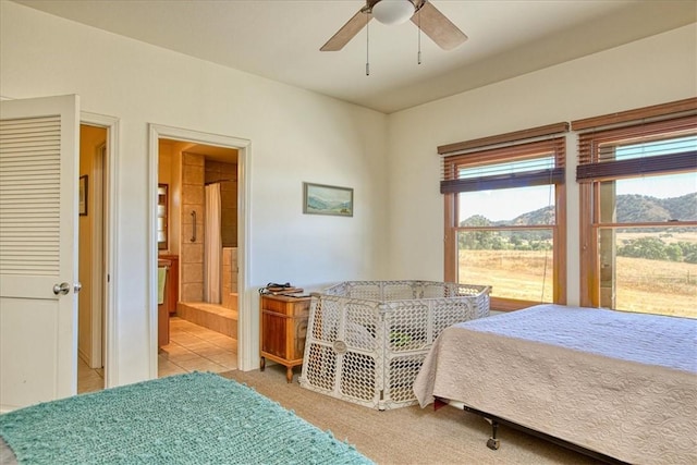 bedroom with a mountain view, ceiling fan, and connected bathroom