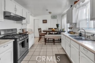 kitchen with white cabinetry, light tile patterned flooring, stainless steel gas stove, range hood, and sink