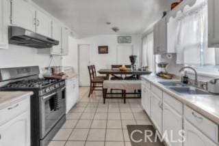 234 E Raymond St, Compton, CA 90220 - kitchen featuring gas range, under cabinet range hood, light tile patterned floors, a sink, and white cabinets
