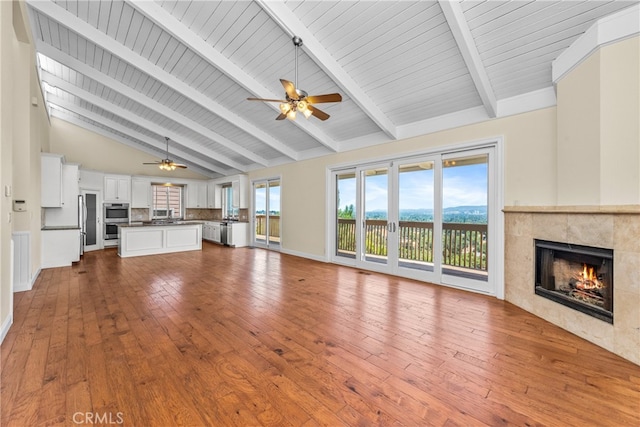 unfurnished living room with high vaulted ceiling, a tile fireplace, ceiling fan, beamed ceiling, and hardwood / wood-style flooring