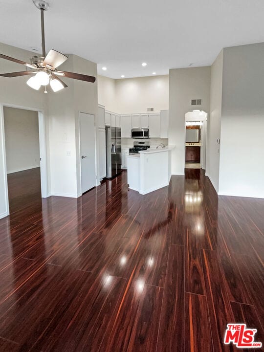 unfurnished living room with ceiling fan, a towering ceiling, and dark wood-type flooring