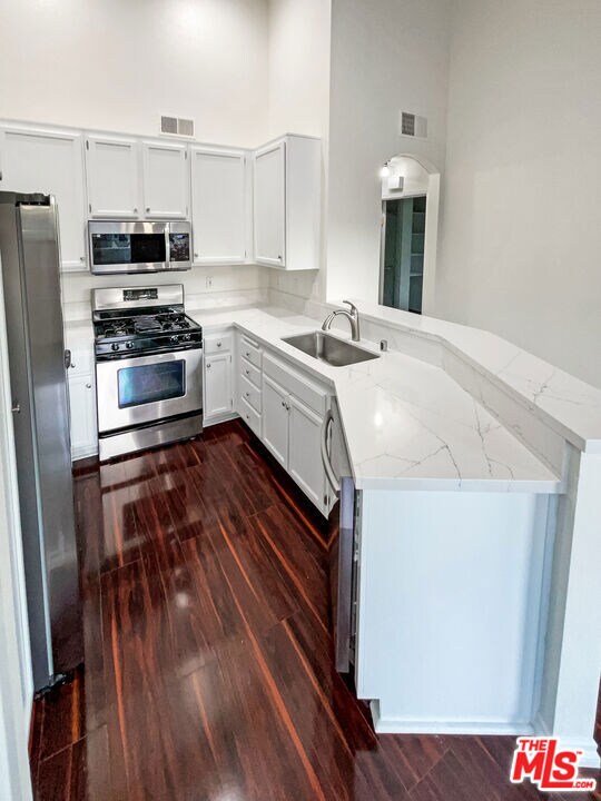 kitchen featuring appliances with stainless steel finishes, kitchen peninsula, sink, and light stone counters