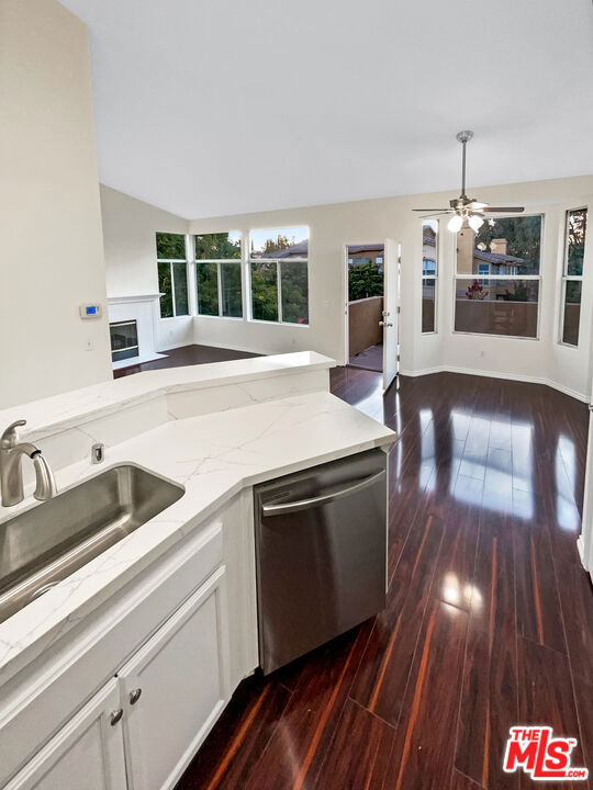 kitchen featuring light stone counters, ceiling fan, stainless steel dishwasher, white cabinetry, and dark hardwood / wood-style flooring