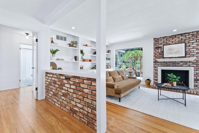 living room featuring crown molding, a brick fireplace, built in shelves, and light wood-type flooring