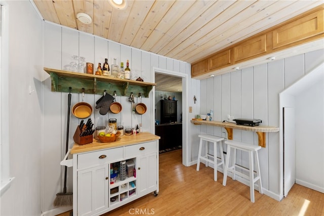 kitchen with wood walls, white cabinetry, wooden ceiling, and light wood-type flooring