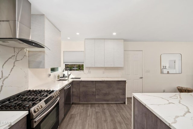 kitchen featuring appliances with stainless steel finishes, sink, white cabinets, light stone counters, and wall chimney exhaust hood