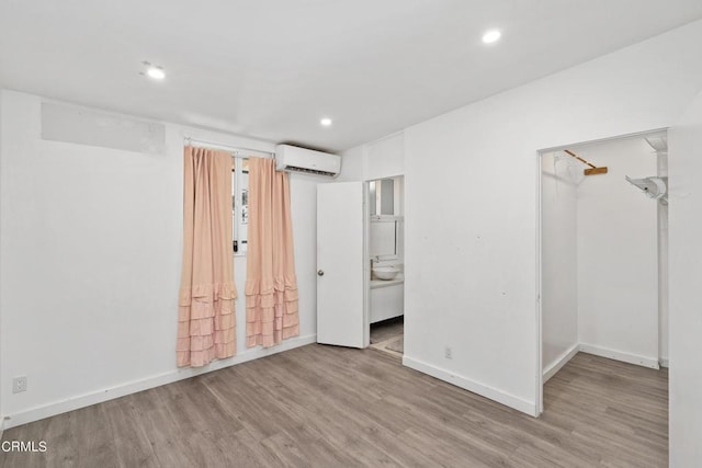 unfurnished bedroom featuring a walk in closet, a wall mounted AC, ensuite bath, and light hardwood / wood-style flooring