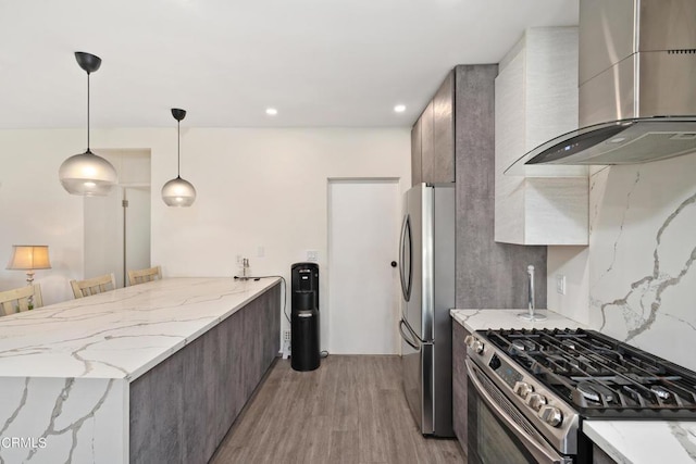 kitchen featuring appliances with stainless steel finishes, pendant lighting, a breakfast bar area, light hardwood / wood-style floors, and wall chimney range hood