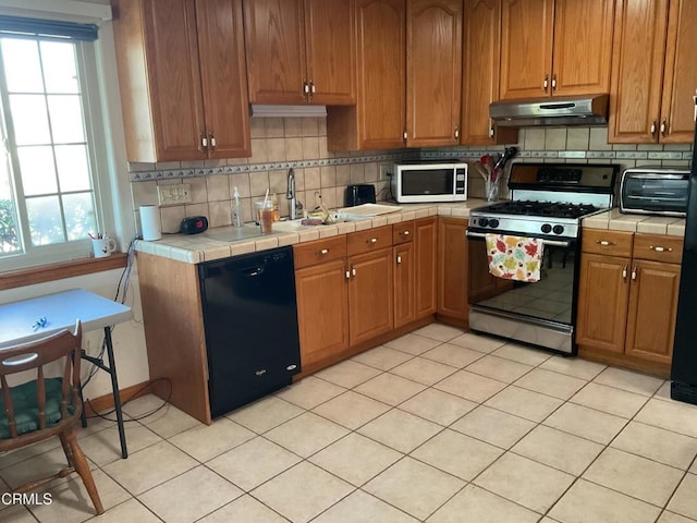 kitchen featuring backsplash, gas range, tile counters, and dishwasher