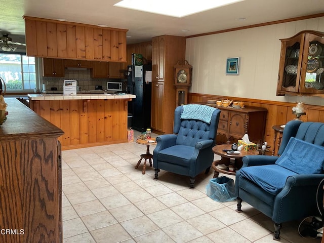 kitchen with wood walls, backsplash, black fridge, tile counters, and light tile patterned flooring