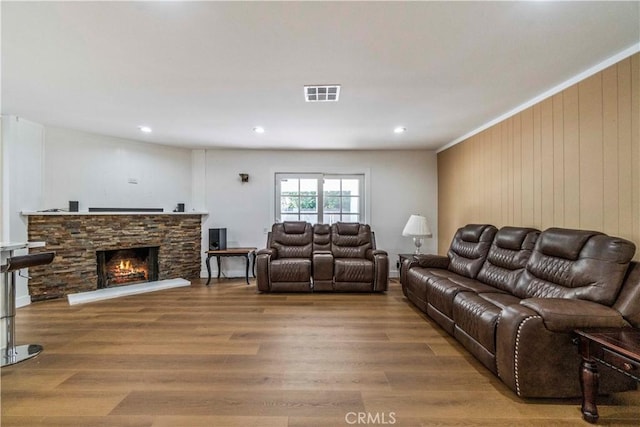 living room featuring hardwood / wood-style flooring, a stone fireplace, crown molding, and wooden walls