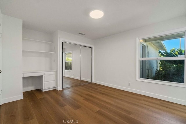 unfurnished bedroom with multiple windows, a closet, dark hardwood / wood-style flooring, and built in desk