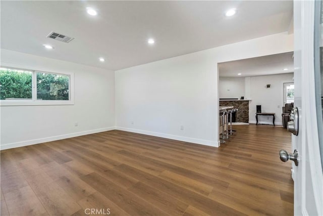 unfurnished room featuring dark hardwood / wood-style flooring, a stone fireplace, and a healthy amount of sunlight