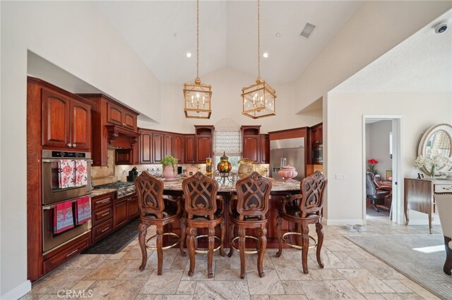 kitchen featuring hanging light fixtures, a kitchen island with sink, high vaulted ceiling, a kitchen bar, and built in appliances