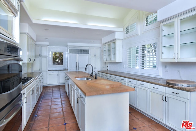 kitchen featuring white cabinets, sink, an island with sink, and tasteful backsplash