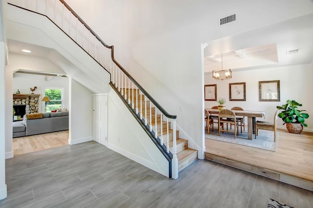 stairway with a stone fireplace, wood-type flooring, and an inviting chandelier