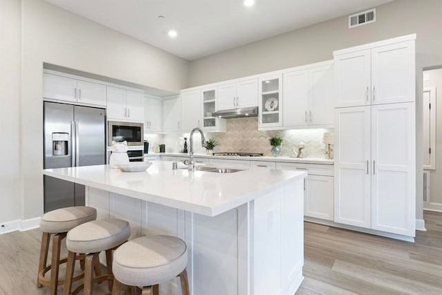 kitchen featuring an island with sink, stainless steel appliances, white cabinetry, and a breakfast bar area