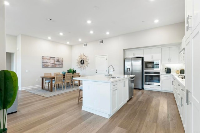 kitchen featuring appliances with stainless steel finishes, light hardwood / wood-style floors, white cabinets, a center island with sink, and sink