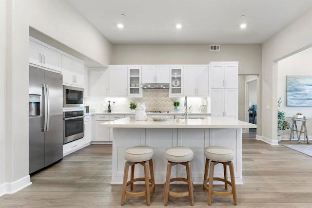 kitchen featuring appliances with stainless steel finishes, light hardwood / wood-style floors, a kitchen island with sink, and white cabinets