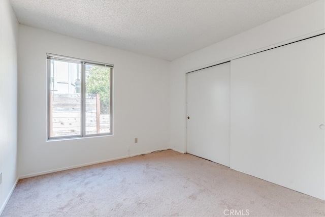 unfurnished bedroom with light colored carpet, a textured ceiling, and a closet