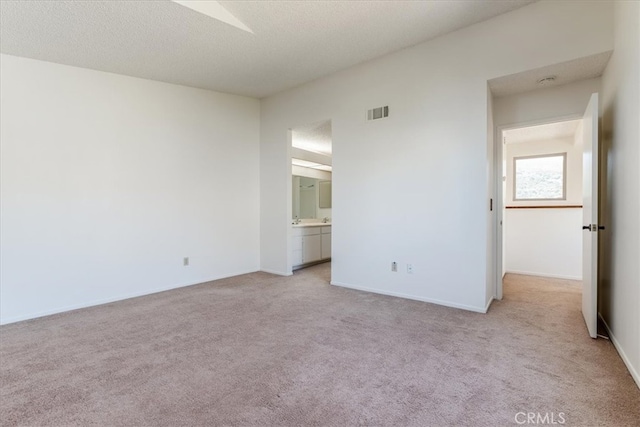 unfurnished bedroom with connected bathroom, a textured ceiling, and light colored carpet