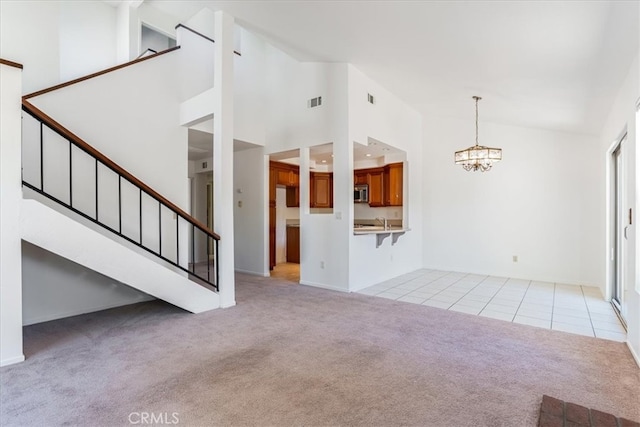 unfurnished living room with high vaulted ceiling, a chandelier, light colored carpet, and sink