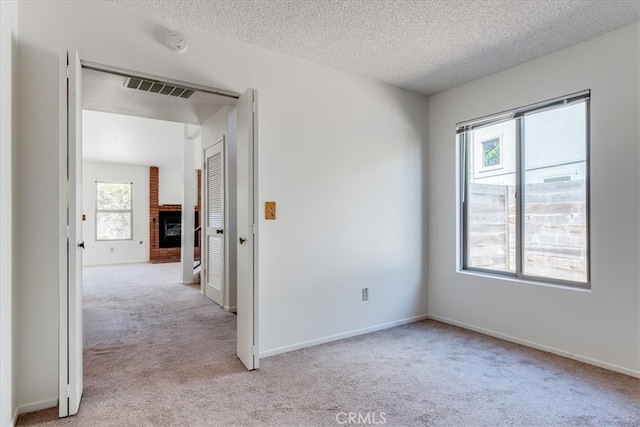 carpeted spare room with a textured ceiling, a fireplace, and a healthy amount of sunlight