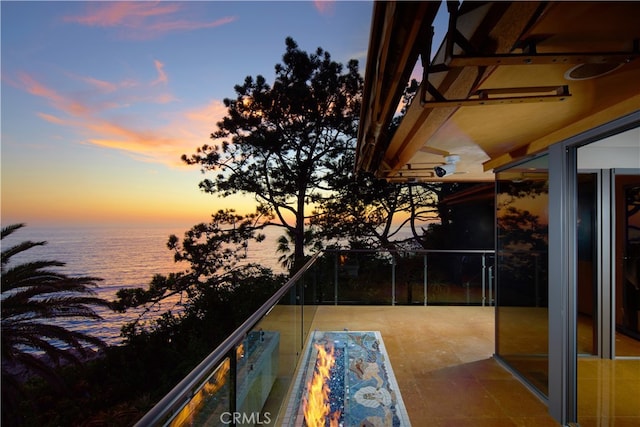 balcony at dusk featuring a water view and a fire pit